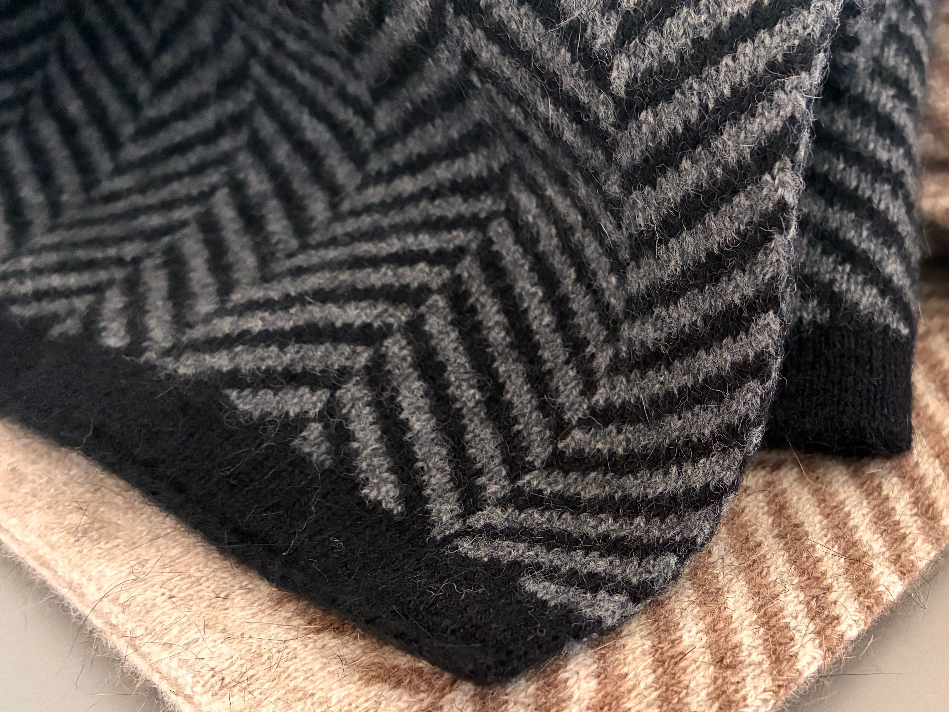 Close-up of two parquet-patterned scarves in black and beige on a light surface.