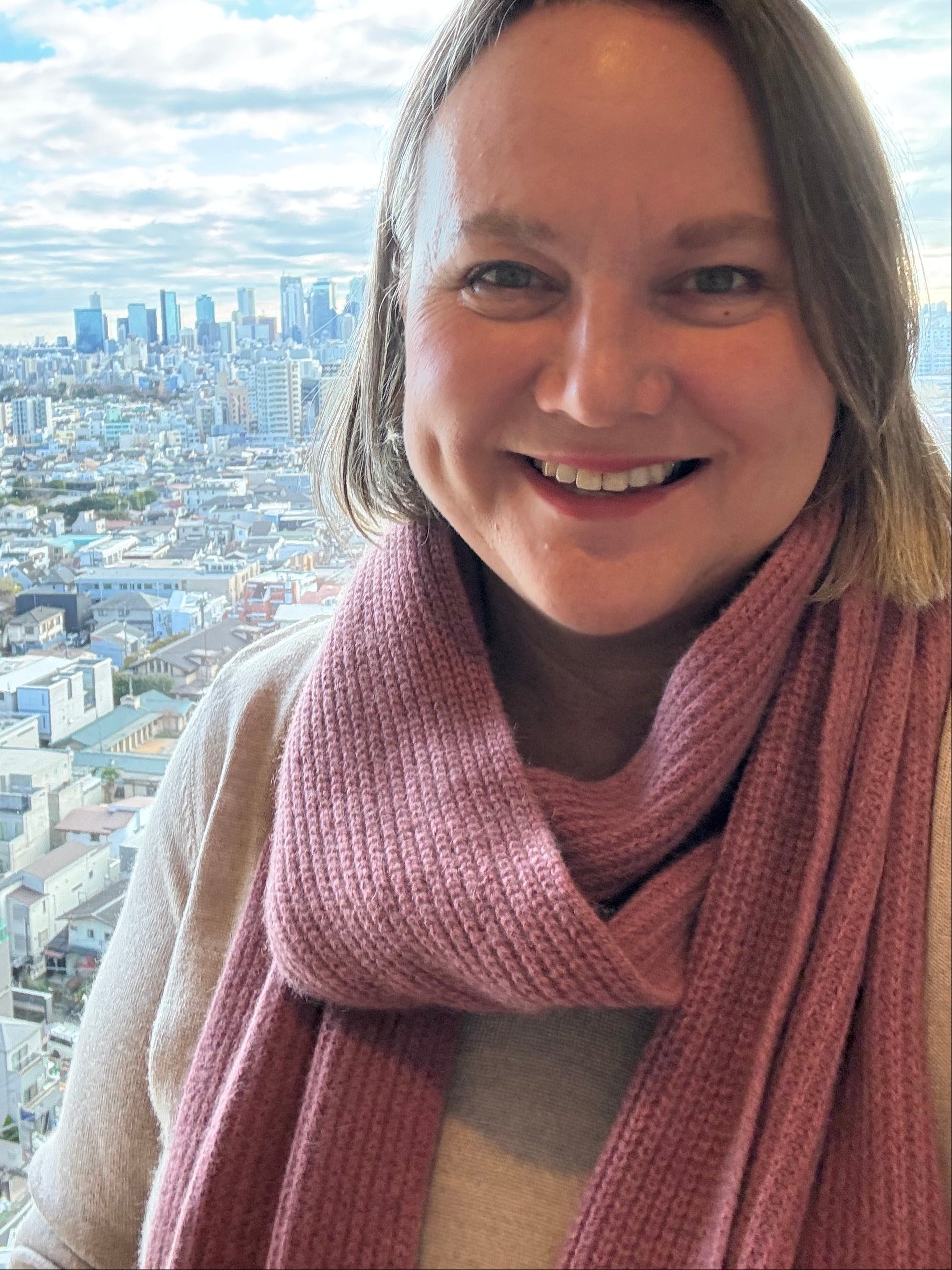 Person wearing a pink sweater with a cityscape view outside a window