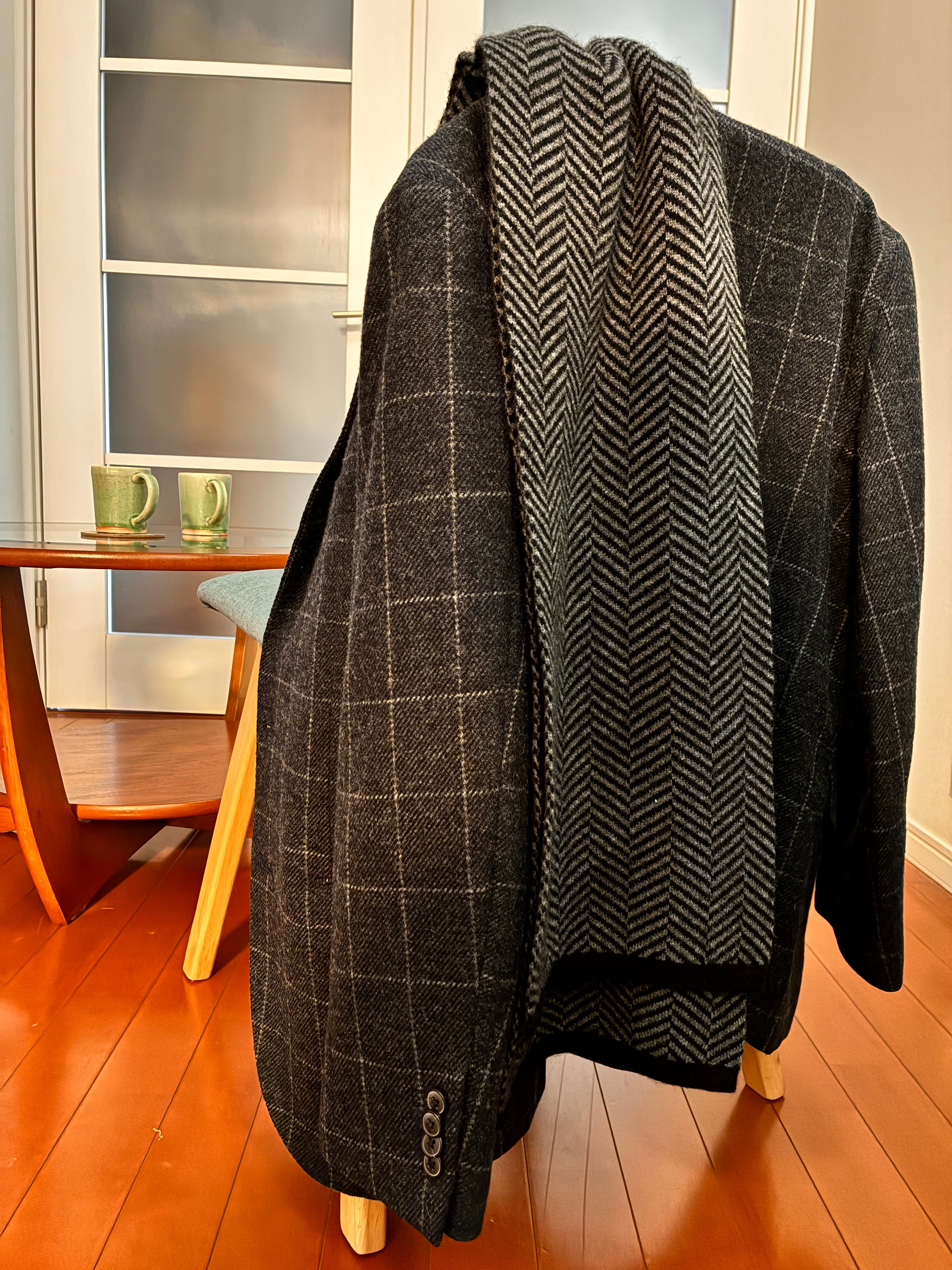 Gray checkered coat draped over a chair in a room with wooden floor and glass door.