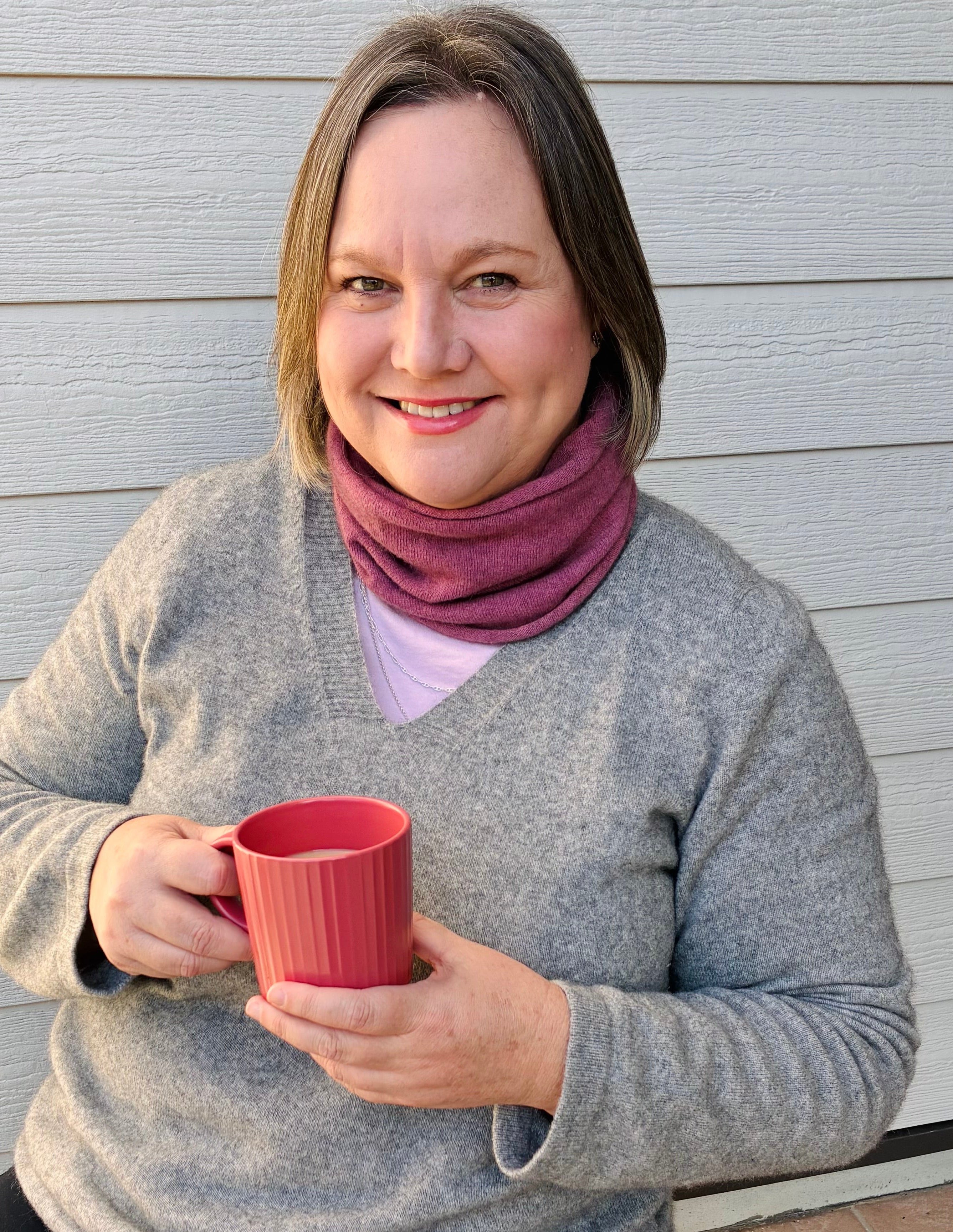Mature woman wearing magnolia pink Neckwarmer and silver merino possum sweater with cup of tea 